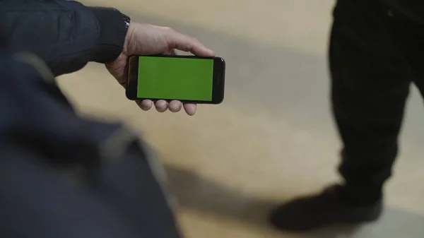 Gros plan de jeunes mains masculines tenant un smartphone moderne avec écran tactile vert. Mans main montre smartphone mobile avec écran vert à son ami — Photo