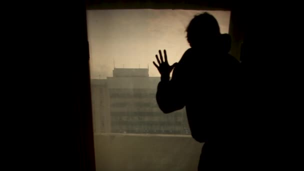 Uomo in piedi con la mano alla finestra vista posteriore. Un filmato. Silhouette uomo guardando fuori dalla finestra con la luce nella stanza . — Video Stock