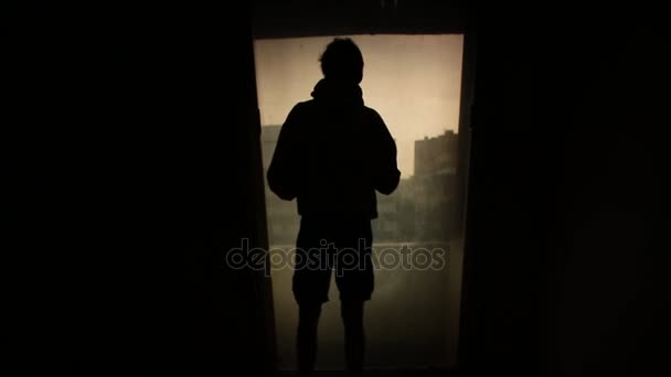 Σιλουέτα άνθρωπος ψάχνει έξω από το παράθυρο με το φως στο δωμάτιο. Μήκος σε πόδηα. Σιλουέτα ενός νεαρού μόνος στο δωμάτιο. Έννοια της μοναξιάς — Αρχείο Βίντεο