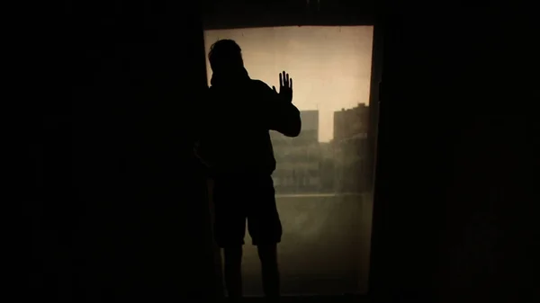 실루엣 남자 방에 빛으로 창 밖을 보면서. 영상입니다. 방에 외로운 젊은이의 실루엣. 외로움의 개념 — 스톡 사진