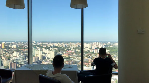 Twee mans met lunch in moderne restaurant met panoramisch raam en uitzicht op de prachtige stad. vriend genieten van elkaars bedrijf terwijl het hebben van feestelijk diner in restaurant met panoramische ramen — Stockfoto
