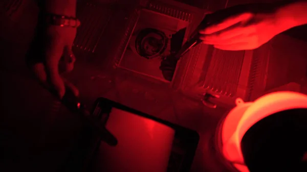 Σκοτεινού θαλάμου εκτύπωσης διαδικασία φωτογράφο με χρήση μεγεθυντικών συσκευών να παράγουν φωτογραφικές εκτυπώσεις. Γυναίκα που εργάζεται σε ένα κόκκινο σκοτεινό δωμάτιο — Φωτογραφία Αρχείου