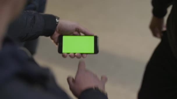 Κοντινό πλάνο της νεαρά αρσενικά χέρια που κρατούν σύγχρονο smartphone με οθόνη αφής πράσινο. Επανδρώνει το χέρι δείχνει κινητά smartphone με πράσινη οθόνη με τον φίλο του — Αρχείο Βίντεο