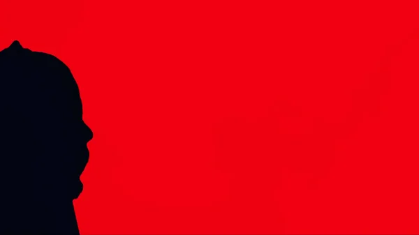 黒フード、赤い背景の男のシルエット。赤いカーテンの背景を持つフードに目に見えない人間の肖像 — ストック写真