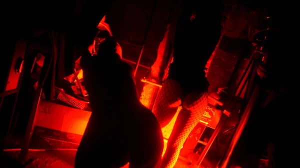 Utilisation du fouet en cuir pour les jeux BDSM en chambre rouge avec lumière rouge. Belle femme nue posant en lingerie en cuir. Deux belles filles sexy en robe de latex posant près du mur lumineux. Feu rouge. Passion — Photo