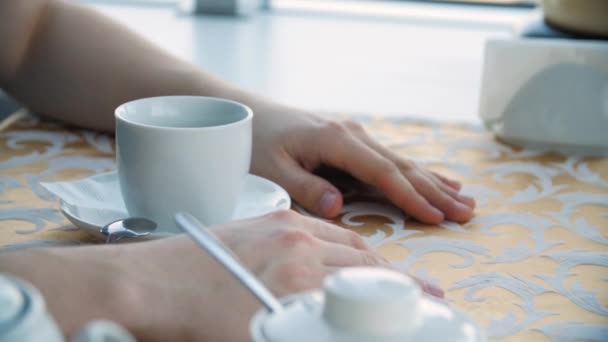 Feche as mãos dos homens com uma xícara de café na mesa e no fundo da janela. Businessman coffee break closeup, mãos com copo americano na mesa de madeira, close-up — Vídeo de Stock