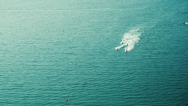 Вид сверху на человека, катающегося на водных мотоциклах с большим количеством брызг в голубой прозрачной океанской воде. Концепция отпуска. вид сверху на океан, катание на водных лыжах — стоковое фото