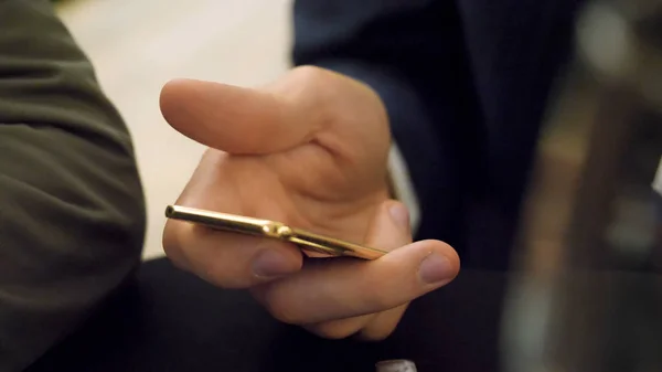 Homem segurando o smartphone dourado. Um smartphone de cor dourada foi mantido por mãos ocupadas atualizando em redes sociais — Fotografia de Stock