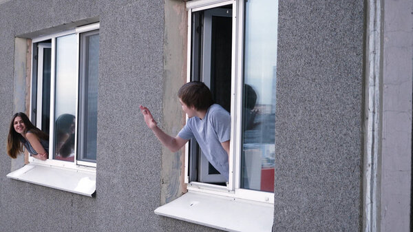 Young man talks with a neighbor through the window. Young man smokes a cigarette and talks with a neighbor from his window