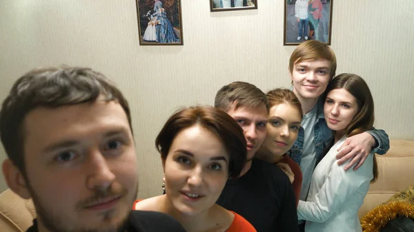 Happy friends enjoying time together and making a selfie. Group of young friends taking selfie in home interior. Handsome guy is making selfie with his friends at the party on his phones camera — Stock Photo, Image