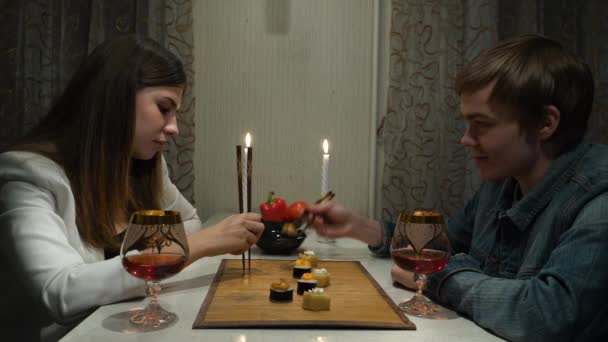 Casal jovem tendo jantar romântico com seu namorado, beber vinho e comer rolos juntos em casa. Menina com um cara em um encontro romântico em casa — Vídeo de Stock