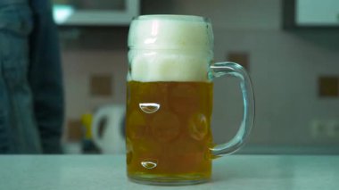 Bir adam close-up bir bardak bira masadan alır. Adam bir bardak bira tablosundan alır. Ev. Bir adam mutfakta bir bardak bira tablosundan alır