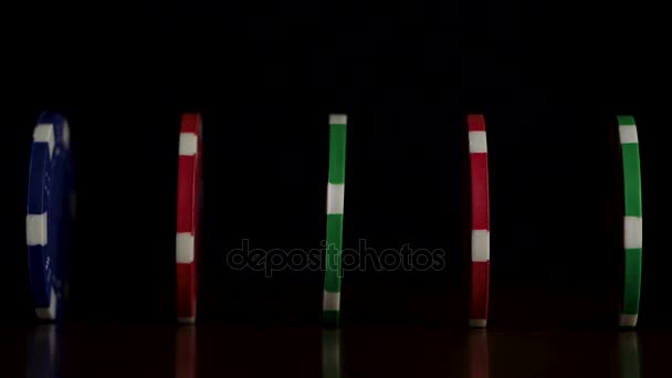 Las fichas de póquer están en una fila sobre un fondo negro, un efecto dominó. Jugar fichas de póquer están sobre la mesa, un símbolo del casino — Vídeos de Stock
