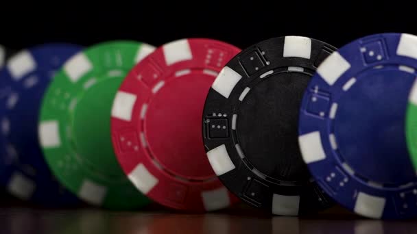 Poker chips stand in a row on a black background, a Domino effect. Playing poker chips are on the table, a symbol of casino — Stock Video