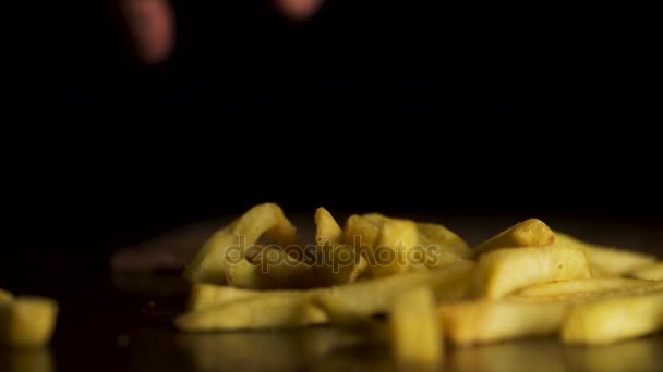 La mano de los hombres con entusiasmo quita las papas fritas de la mesa. Patatas en rodajas en una tabla de cortar. Vista de cerca. Deliciosas papas fritas, bellamente decoradas, está sobre la mesa, concepto de comida rápida — Vídeo de stock