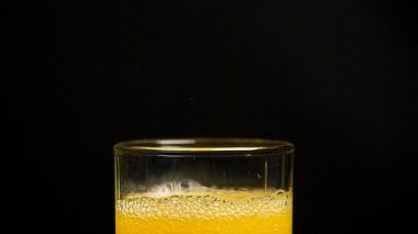 Portakal suyu dökme. Ağır çekim. Gazlı portakal suyu bir bardak dökülür. Ağır çekimde bardakta portakal suyu tozu dökme, siyah arka plan