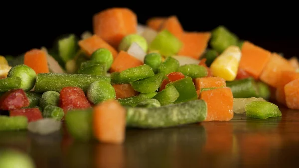 Gehakte groenten. Plakjes rode en groene paprika's, wortelen, groene bonen, erwten, ui, maïs vallen op zwarte achtergrond. Slow-Motion. Gehakte groenten vallen op zwarte achtergrond Stockfoto