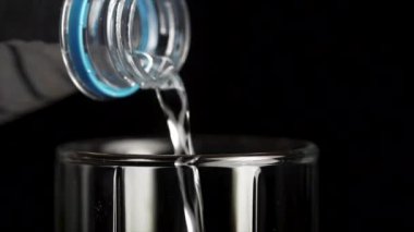 Su şişesinden üzerinde siyah bir arka plan şeffaf cam bardağa dökülür. Bir cam şişe içine su dökülür, yakın çekim
