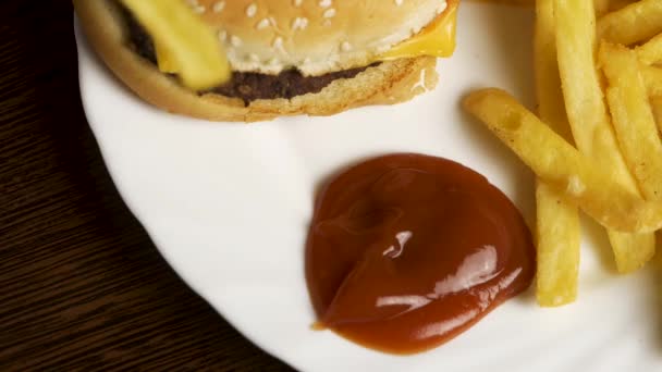 El joven moja papas fritas en ketchup. Papas fritas con ketchup y hamburguesa. Hamburguesa con papas fritas en un plato blanco. Deliciosa comida rápida — Vídeos de Stock