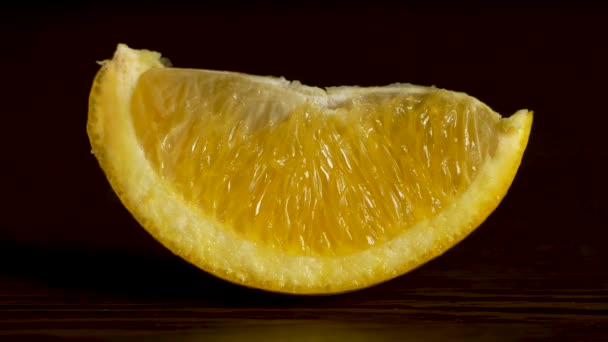 Juicy Fresh Fruit Orange Segments Against a Black Background. Rebanada fresca y jugosa de naranja descansa sobre la mesa sobre un fondo negro, el concepto de una nutrición adecuada — Vídeo de stock