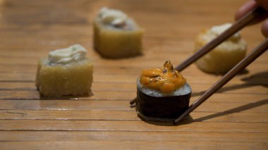 Japon suşi rulo ve yemek çubukları. Tablo Restoran, suşi roll bölümünü alarak suşi roll yemek çubukları kullanarak yemek yemek çubukları yakın çekim. Suşi dilim görünümünü yakın çekim