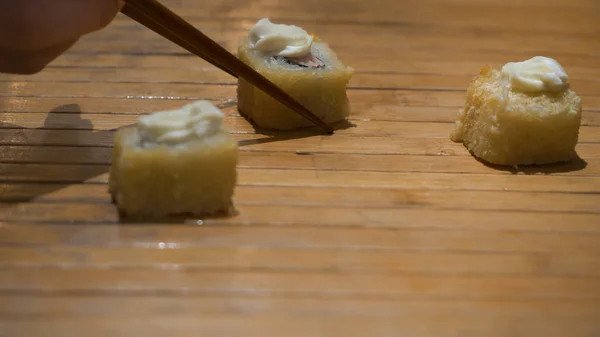 Sushi rotoli giapponesi e bacchette. primo piano di bacchette prendendo porzione di rotolo di sushi sul ristorante tavolo, mangiare rotolo di sushi con le bacchette. Vista ravvicinata della fetta di sushi — Foto Stock