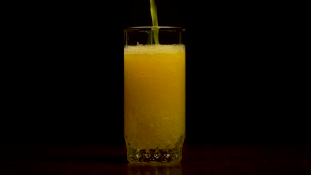 Soda naranja vaso grande, vaso desbordante de soda naranja primer plano con burbujas aisladas sobre fondo negro. El refresco de naranja se vierte en un vaso — Vídeo de stock