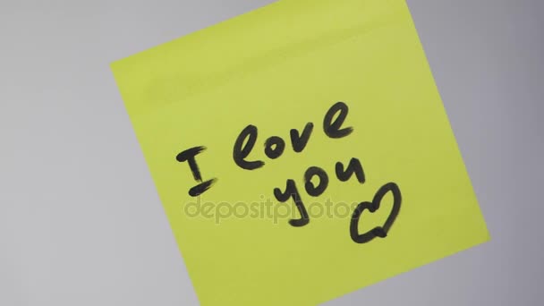 Dibujar "Te amo" en papel amarillo. Inscripción en la pegatina Te amo sobre fondo blanco — Vídeo de stock
