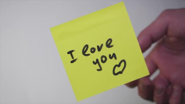 Desenhar "Amo-te" em papel amarelo. Inscrição no adesivo Eu te amo no fundo branco — Vídeo de Stock