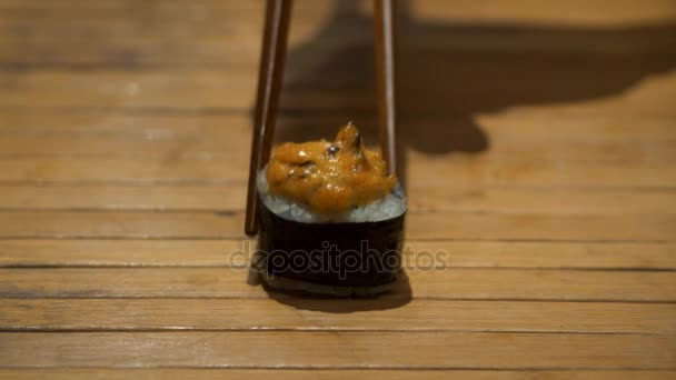 Primer plano de palillos que toman parte del rollo de sushi en el restaurante de la mesa, comiendo rollo de sushi usando palillos. Rollo de sushi sobre fondo de madera — Vídeo de stock