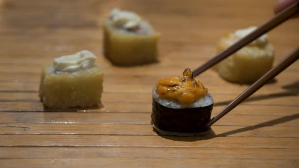 Primer plano de palillos que toman parte del rollo de sushi en el restaurante de la mesa, comiendo rollo de sushi usando palillos. Rollo de sushi sobre fondo de madera — Vídeo de stock