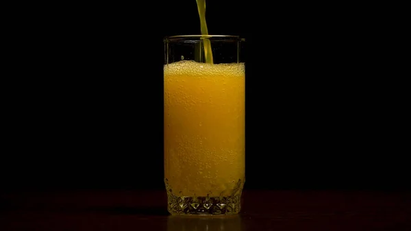 Orange Soda großes Glas, überfließendes Glas aus orangefarbenem Soda Nahaufnahme mit Blasen isoliert auf schwarzem Hintergrund. orangefarbenes Getränk. Zeitlupe. kohlensäurehaltiges Orangengetränk wird in ein Glas gegossen. — Stockfoto