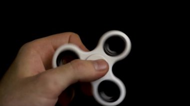 Erkek el ile izole siyah arka plan üzerine beyaz spinner. Siyah arka plan üzerine beyaz topluca spinner aygıt. Bir beyaz el spinner topluca oyuncakla oynamak. Adam beyaz spinner el siyah arka plan üzerine