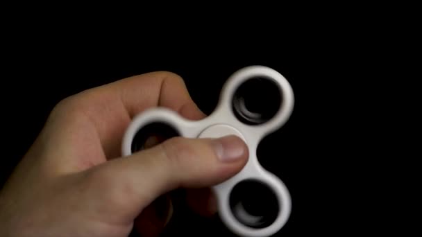 Male hand with white spinner isolated on black background. White fidget spinner device on black background. Playing with a white hand spinner fidget toy. White spinner in man hand on black background — Stock Video
