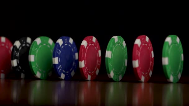 Spelen van poker fiches in reflecterende zwarte achtergrond. Poker chips pokerfiches staan in een rij met donkere achtergrond. Kleurrijke poker chips staande met wit licht en zwarte achtergrond — Stockvideo