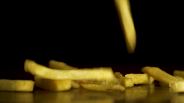 Pommes Frites fallen isoliert auf den Tisch vor schwarzem Hintergrund. Fastfood. Pommes. fliegende Bratkartoffeln auf schwarzem Hintergrund. Haufen Pommes auf schwarzem Hintergrund — Stockvideo