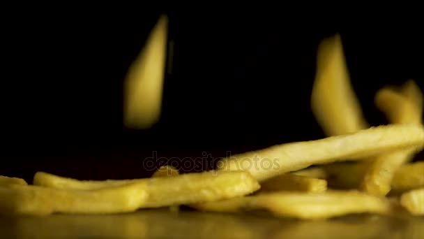 Patatine fritte cadono sul tavolo isolato su sfondo nero. Cibo veloce. Patatine fritte. Patate fritte volanti su sfondo nero. Mucchio di patatine fritte su sfondo nero — Video Stock
