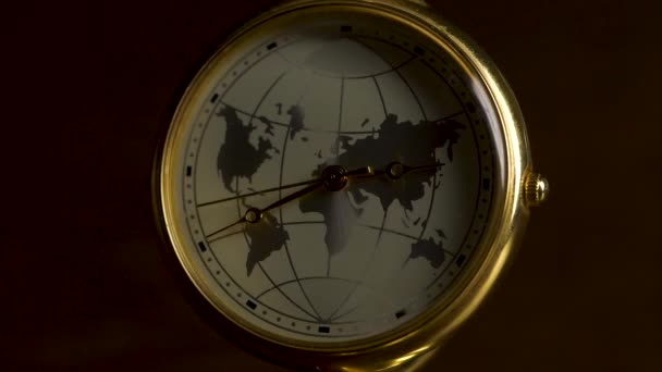 Clock with a picture of planet earth on a wooden table isolated on black background. Detail of a retro clock with timezones and plane. Earth clock with blurred light on dark room. Earth Hour Concept — Stock Video