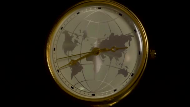 Horloge avec une image de la planète Terre sur une table en bois isolée sur fond noir. Détail d'une horloge rétro avec fuseaux horaires et plan. Horloge terrestre avec lumière floue sur la pièce sombre. Concept d'heure de la Terre — Video