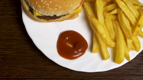 Hambúrguer caseiro fresco com sementes de gergelim preto em prato branco com batatas fritas, servido com molho de ketchup em frasco de vidro sobre a superfície de madeira cinza. Mergulhando batatas fritas em ketchup com mini — Vídeo de Stock