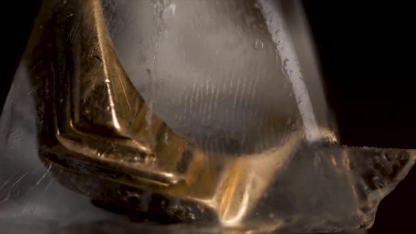 Goldring in Eiswürfel isoliert auf schwarzem Hintergrund. Gold in Eiswürfeln. Goldener Ring mit Eiswürfeln auf Holztisch und schwarzem Hintergrund