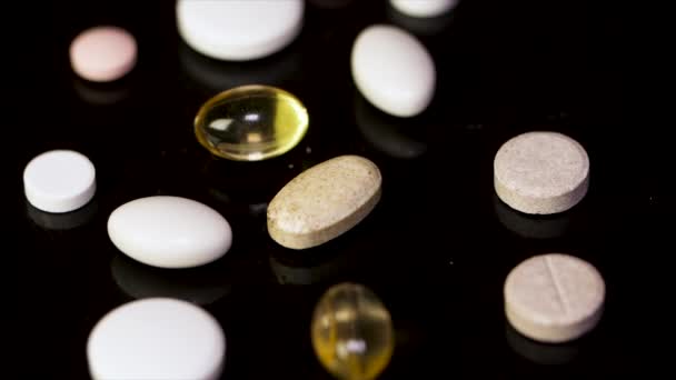 Um monte de comprimidos no fundo preto. pílulas coloridas e agulha no fundo preto, baixo contraste, tecla baixa. Comprimido redondo branco com duas pílulas no fundo. Fundo preto com reflexão — Vídeo de Stock
