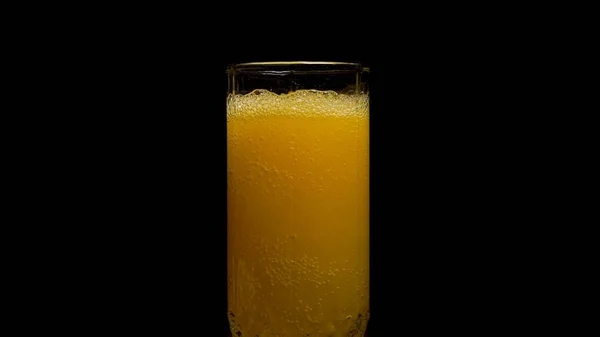 Soda naranja vaso grande, vaso desbordante de soda naranja primer plano con burbujas aisladas sobre fondo negro. Verter Naranja Bebida. A cámara lenta. Bebida de naranja carbonatada se vierte en un vaso . — Foto de Stock