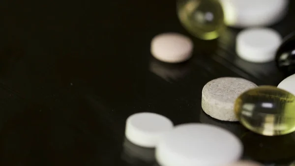 A lot of tablets on the black background. colorful pills and needle on black background, Low contrast, low key. White round tablet with two pills in background. Black background with reflection — Stock Photo, Image
