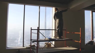 Arkadan Görünüm beyaz kaba pamuklu tulum, şapka ve eldiven bir duvar boya silindiri ile boyama yakışıklı genç ressam. Genç boyama cephe Oluşturucusu alt rulo termal izolasyon işleri