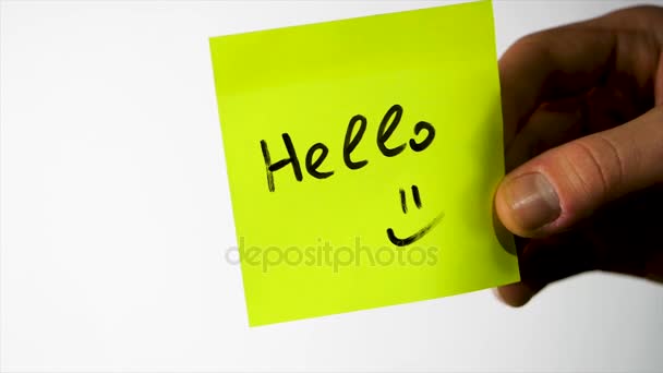 Γεια σας λέξη με χαμογελαστό πρόσωπο σε κίτρινο αυτοκόλλητο χαρτί Σημείωση. Mans χέρι βάλει κενό κίτρινο αυτοκόλλητο που απομονώνονται σε λευκό φόντο. Γεια σου — Αρχείο Βίντεο