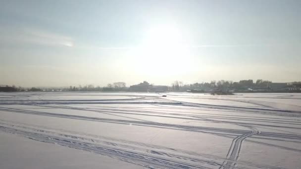 Bilar rida av kurviga isbanan på snöiga sjön på vinterkväll under solnedgången. Flygfoto. En bil kör genom skogen vintern på landsväg. Ovanifrån från drone. — Stockvideo