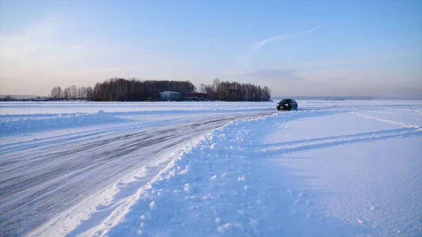 La macchina va nella neve. L'auto guida su una strada innevata fuori città. Grandi corse crossover sulla neve — Foto Stock