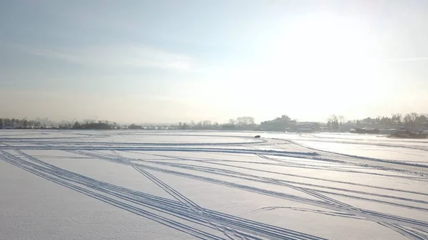 Auto's rijden door bochtige ijs track op besneeuwde lake op winteravond tijdens zonsondergang. Luchtfoto. Een auto rijden door het bos van de winter op de landweg. Bovenaanzicht van drone. — Stockfoto
