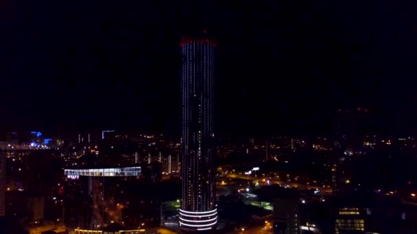 Vista aérea de rascacielos de negocios solitarios por la noche con iluminación y contraluz. Vista aérea del paisaje urbano nocturno de los edificios modernos de rascacielos que brillan con iluminación y luces — Vídeos de Stock